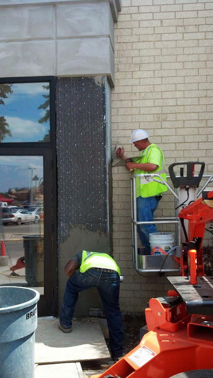 Exterior renovation for repurposing: Construction workers on a lift are applying finishing touches to the exterior of a commercial building, showcasing the improvements and updates as part of the repurposing project.
