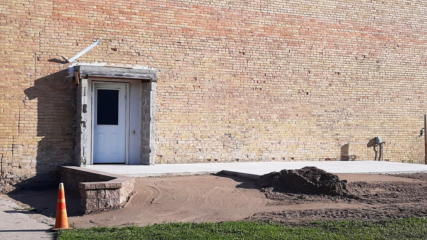The exterior of a brick commercial building undergoing repurposing, with a newly constructed ramp suggesting accessibility upgrades for a potential change in use.