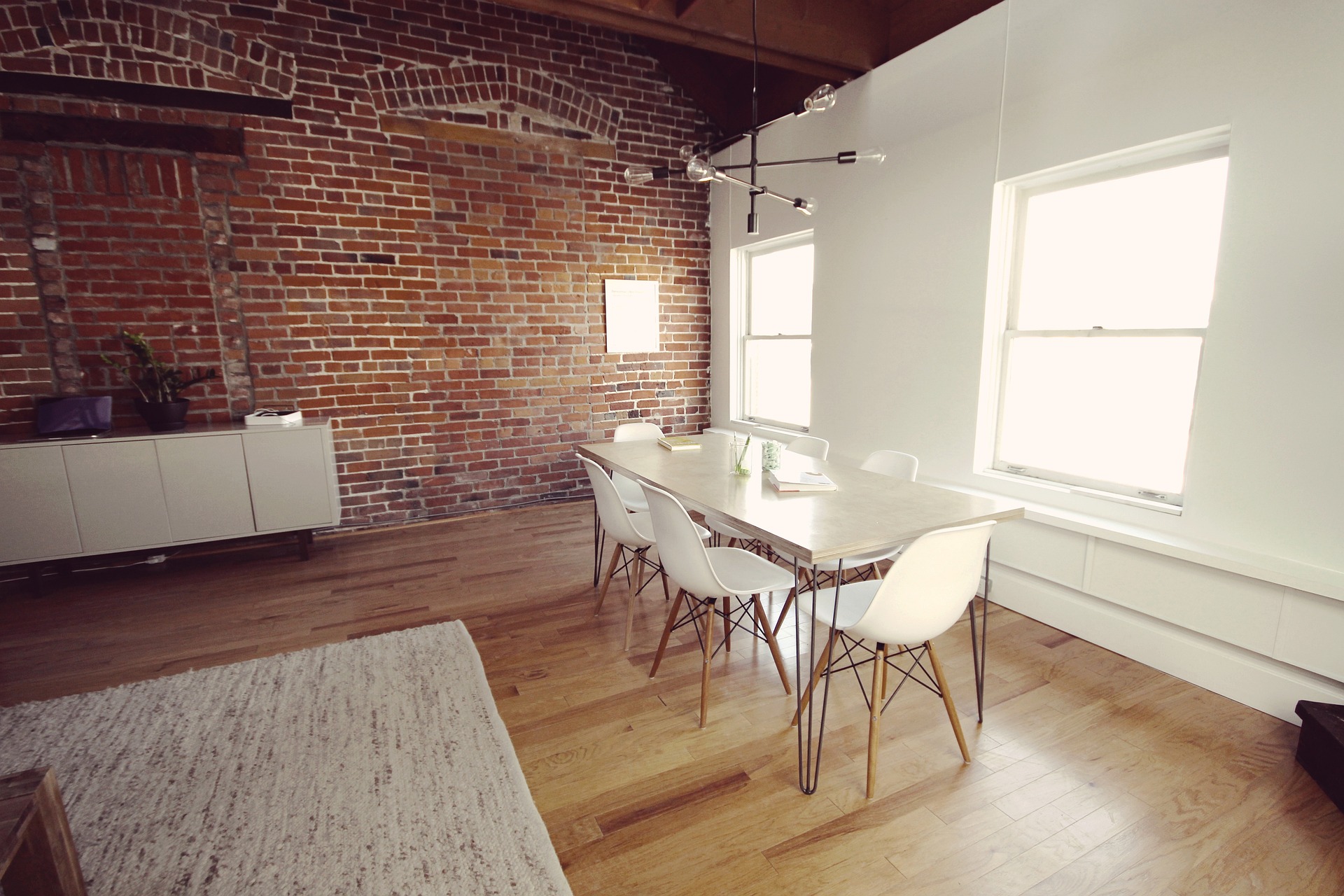 The interior of a loft-style space, a repurposed commercial building, now featuring modern office elements while retaining exposed brick and wooden beams.