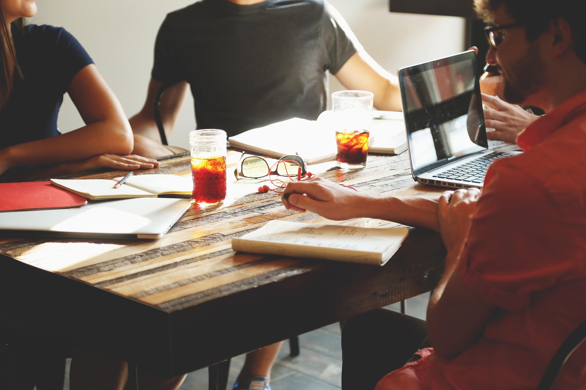 A group of designers collaborateing around a rustic wooden table with drinks, notebooks, and a laptop.